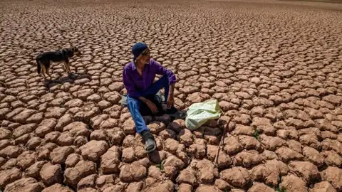 Un homme assis sur un sol craquelé par la sécheresse